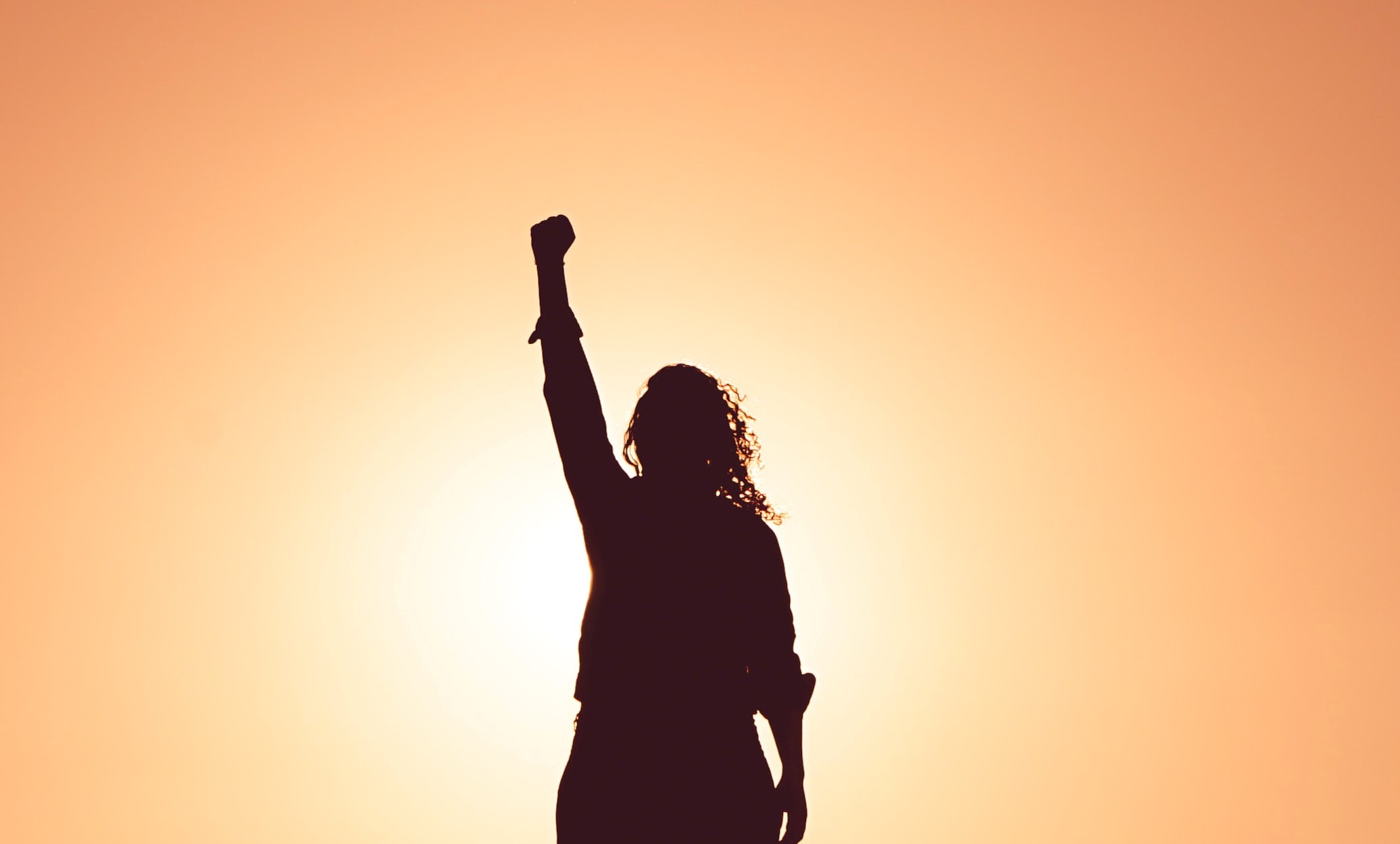 Silhouette of a woman raising her fist against an orange backdrop